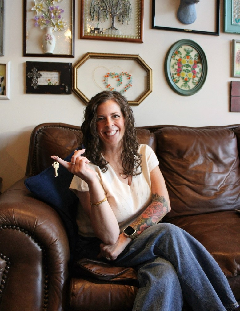 Melissa smiling and holding house keys while seated on a leather couch